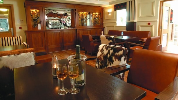 A restaurant with wooden decor, a bar area, and a table with wine glasses and a bottle. - Ashford Court Boutique Hotel (Ennis)