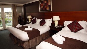 A hotel room with two beds, each with a brown bedspread, white pillows, and a red patterned pillow. There are two bedside tables with lamps, a window with curtains, and a framed artwork on the wall. - Ashford Court Boutique Hotel (Ennis)