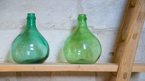 Two green glass bottles on a wooden shelf against a textured wall.