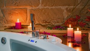 A spa setting with a bathtub, candles, and rose petals.