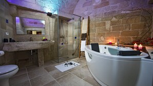 A bathroom with a stone wall, a glass shower enclosure, a white bathtub, and a sink with a mirror above it.
