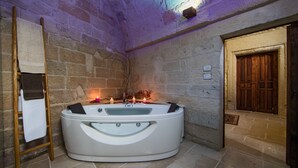 A stone-walled bathroom with a freestanding bathtub, a wooden ladder, and a wooden door.