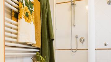 A bathroom with a shower, toilet, and a wooden cabinet with a towel and a potted plant.