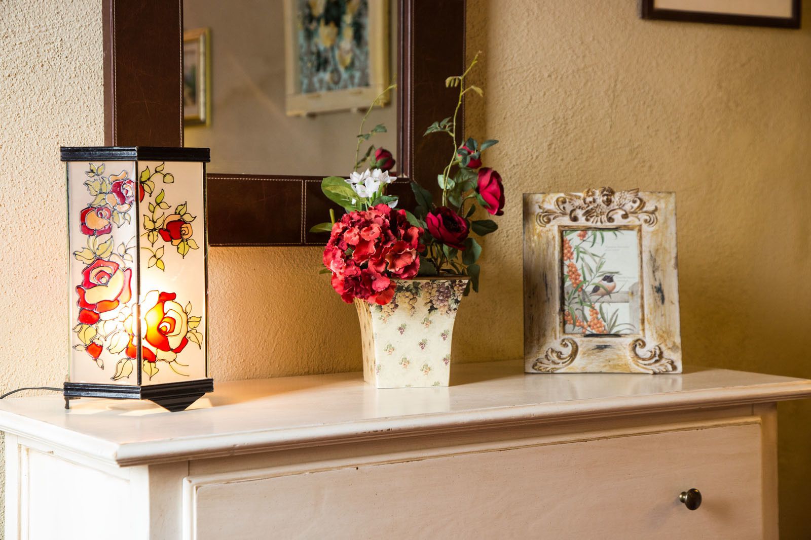 Un jarrón decorativo con flores rojas sobre un tocador blanco.