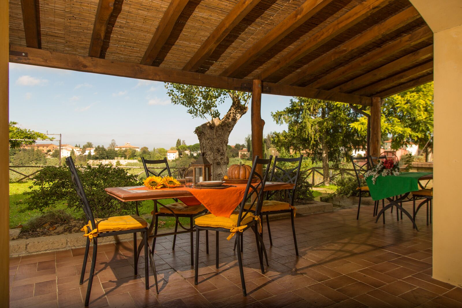 Eine Terrass mit Holz-Pergola, einem Tisch mit gelben Kissen und Blick auf die Landschaft.