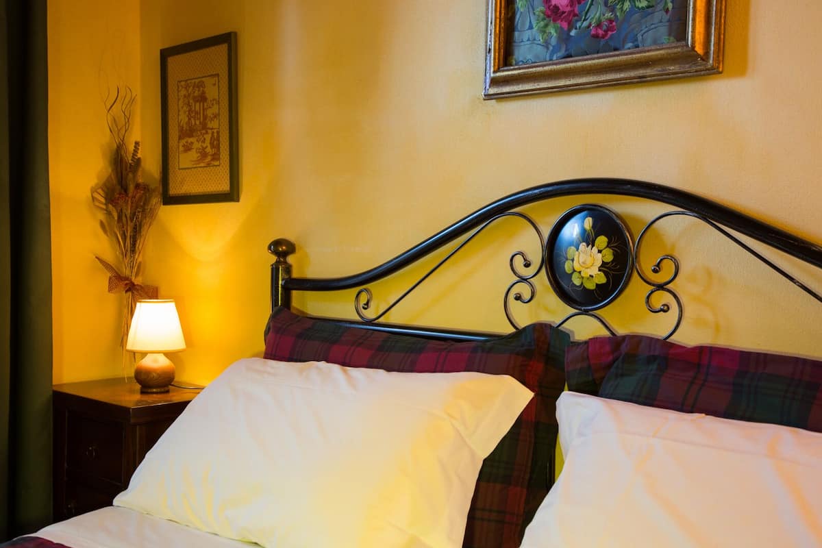 A bed with a metal frame, plaid bedding, and a bedside lamp.