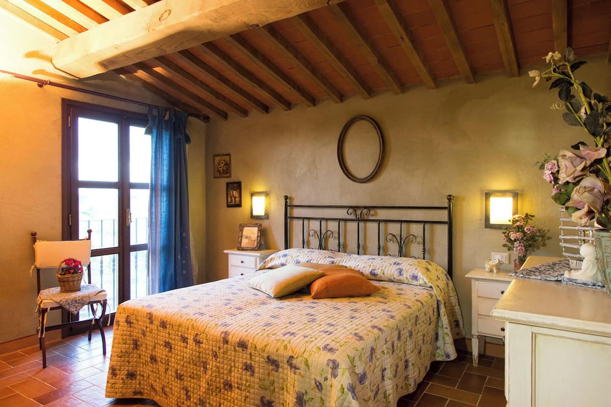 A bedroom with a bed, a chair, a dresser, and a window with curtains.