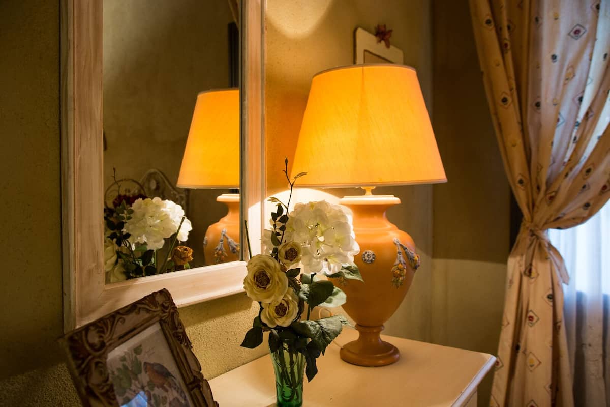 A room with a mirror reflecting a lamp and flowers on a table.