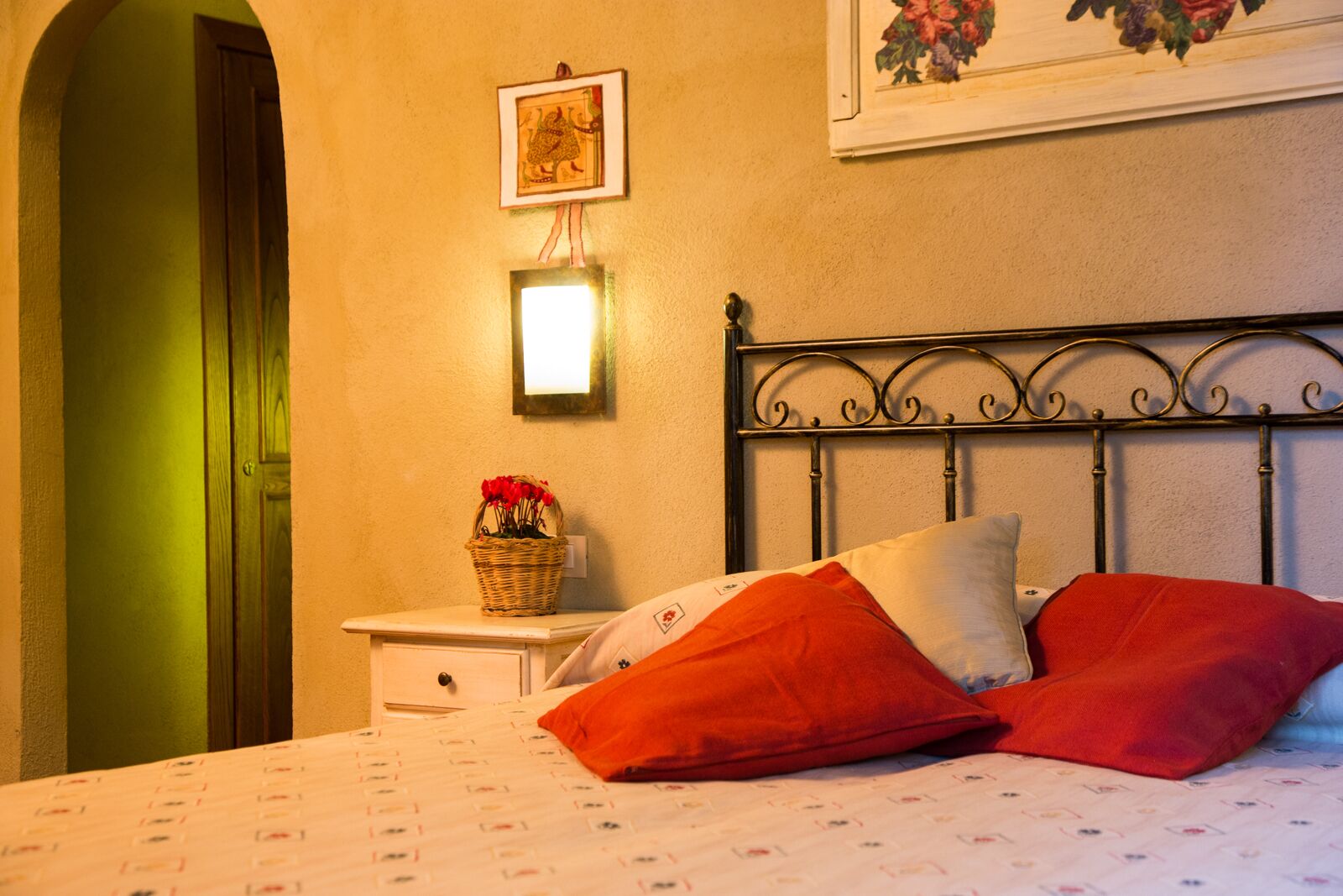 Un dormitorio con cama, mesita de noche, lámpara de pared, cuadro enmarcado y una puerta.