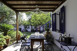 Eine Terrassesituation mit Esstisch, umgeben von Topfpflanzen, und einer Treppe zu einem überdachten Bereich.