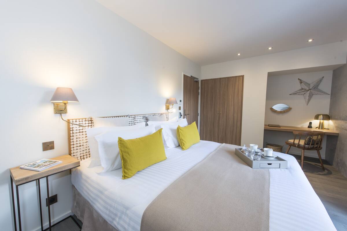 Quarto de hotel com cama, mesas de cabeceira, escrivaninha e cadeira.
