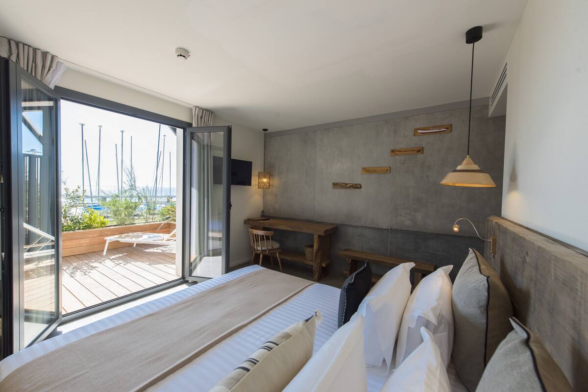 Quarto moderno com uma cama grande, uma escrivaninha e vista para um deck externo através de uma porta de vidro deslizante.