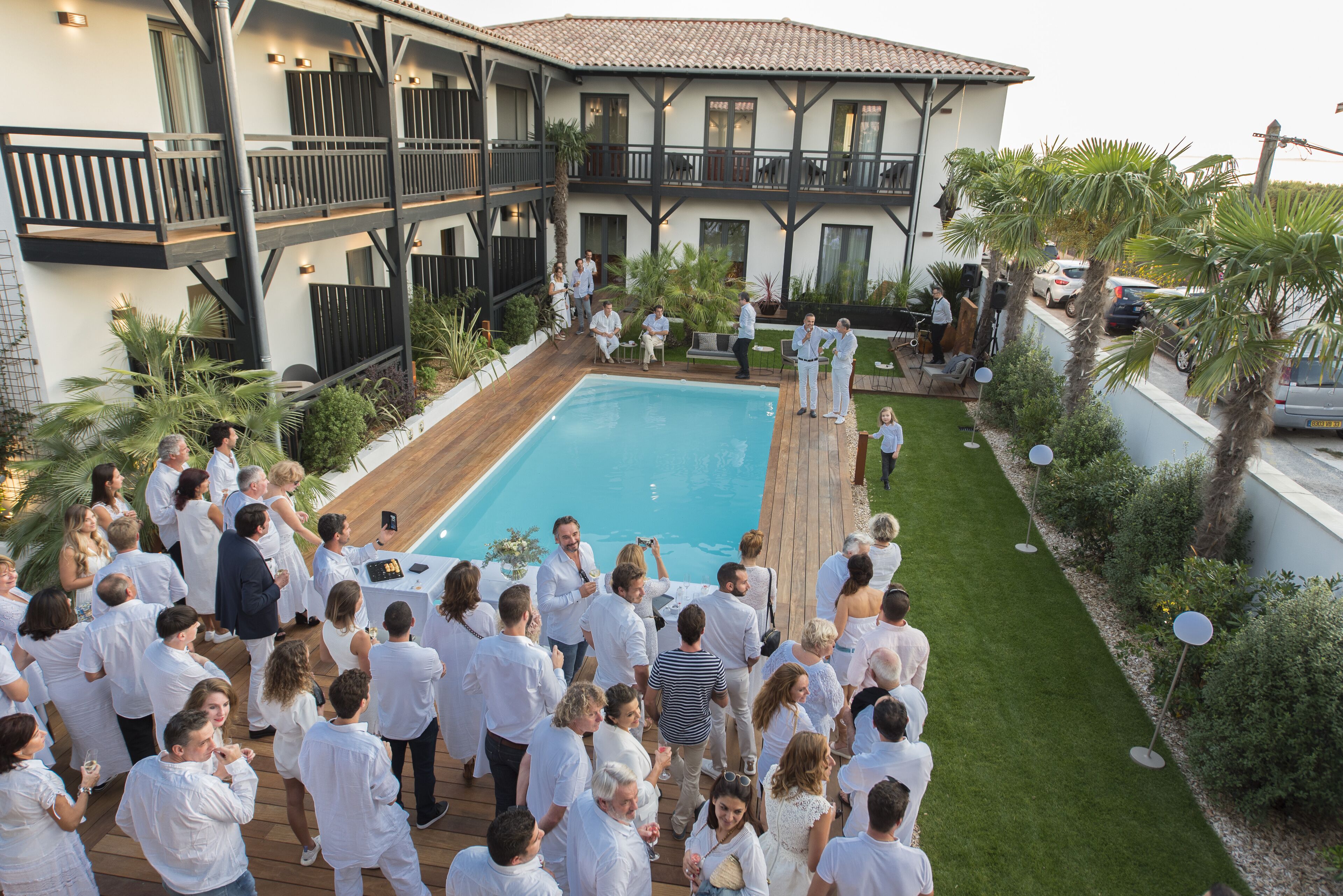 A large outdoor gathering around a pool with a two-story building in the background.