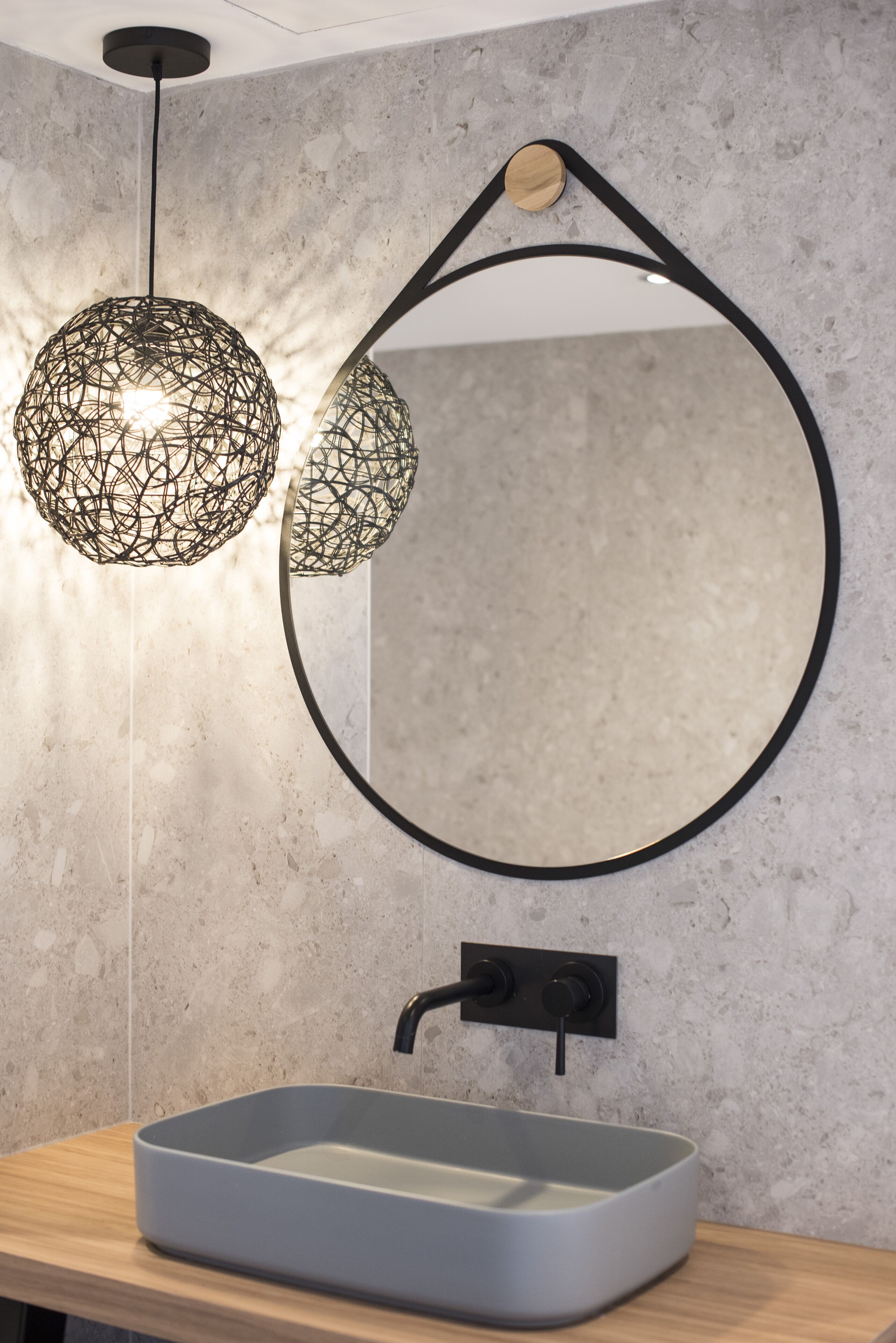 A bathroom with a round mirror, a rectangular sink, and two pendant lights with a woven design.