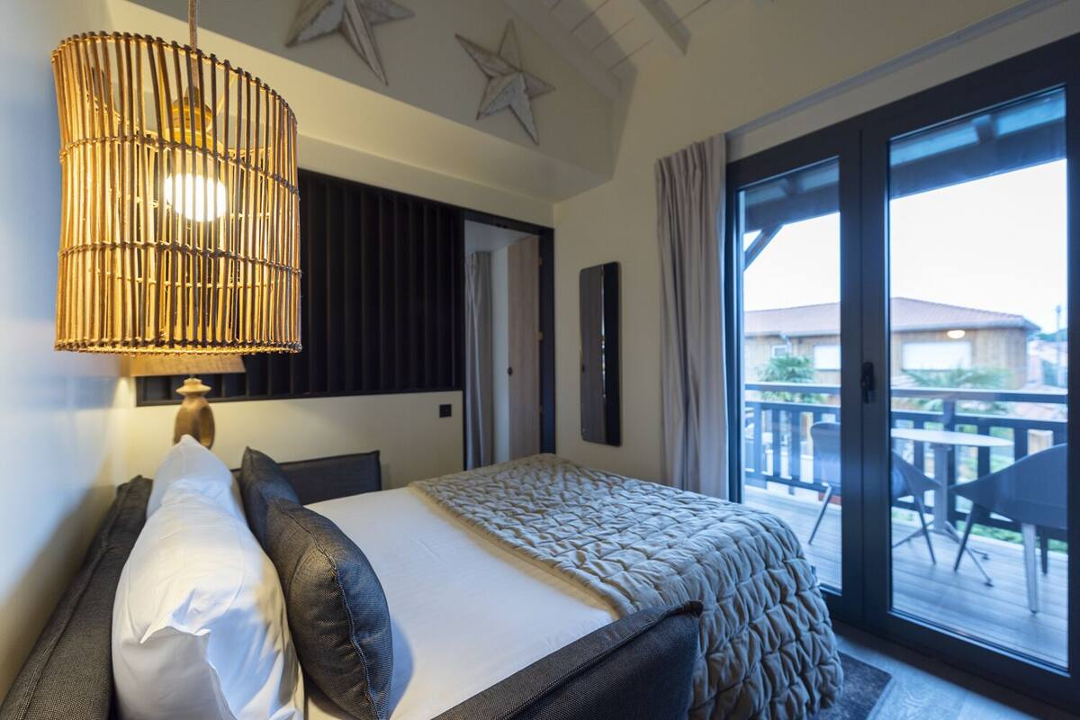 Quarto de hotel com uma cama grande, luminária pendente, vista para o deque externo e decorações de parede em formato de estrela.