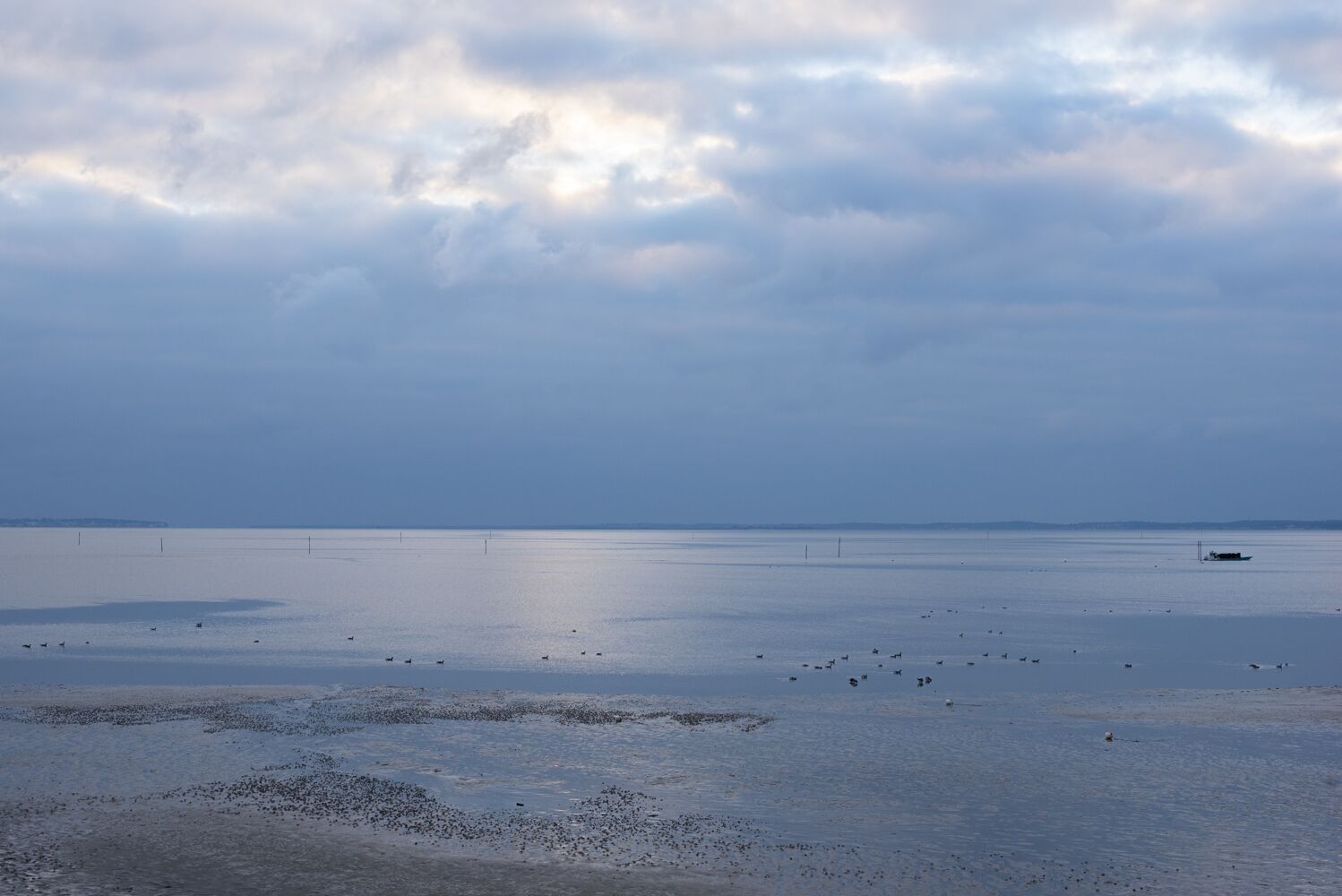A wide, calm body of water with a distant shoreline and a small boat.
