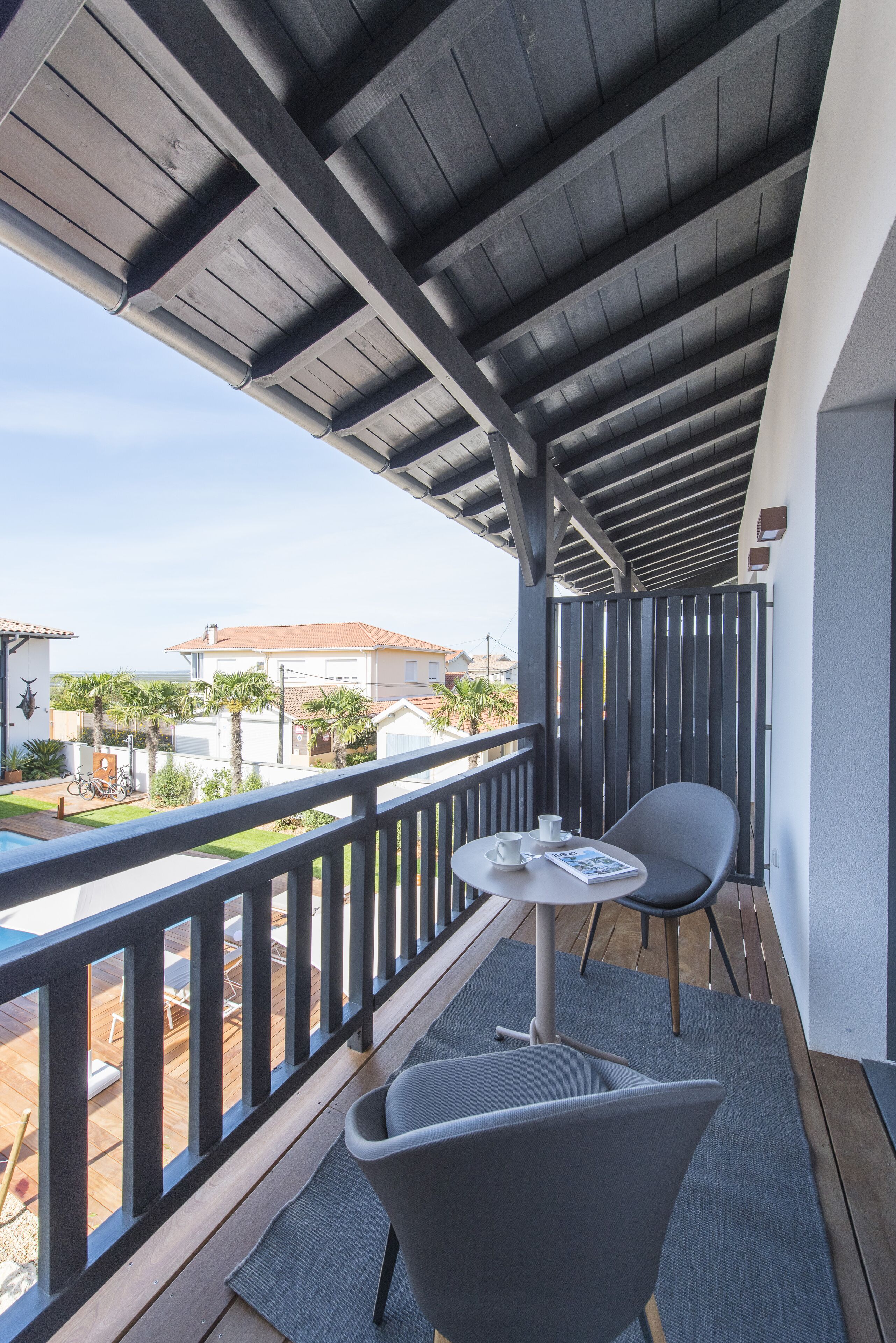 A balcony with a table and chairs, overlooking a residential area with houses and palm trees.
