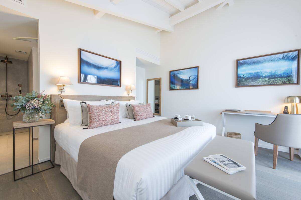 Quarto de hotel moderno com uma cama grande, mesas de cabeceira, uma escrivaninha e obras de arte nas paredes.