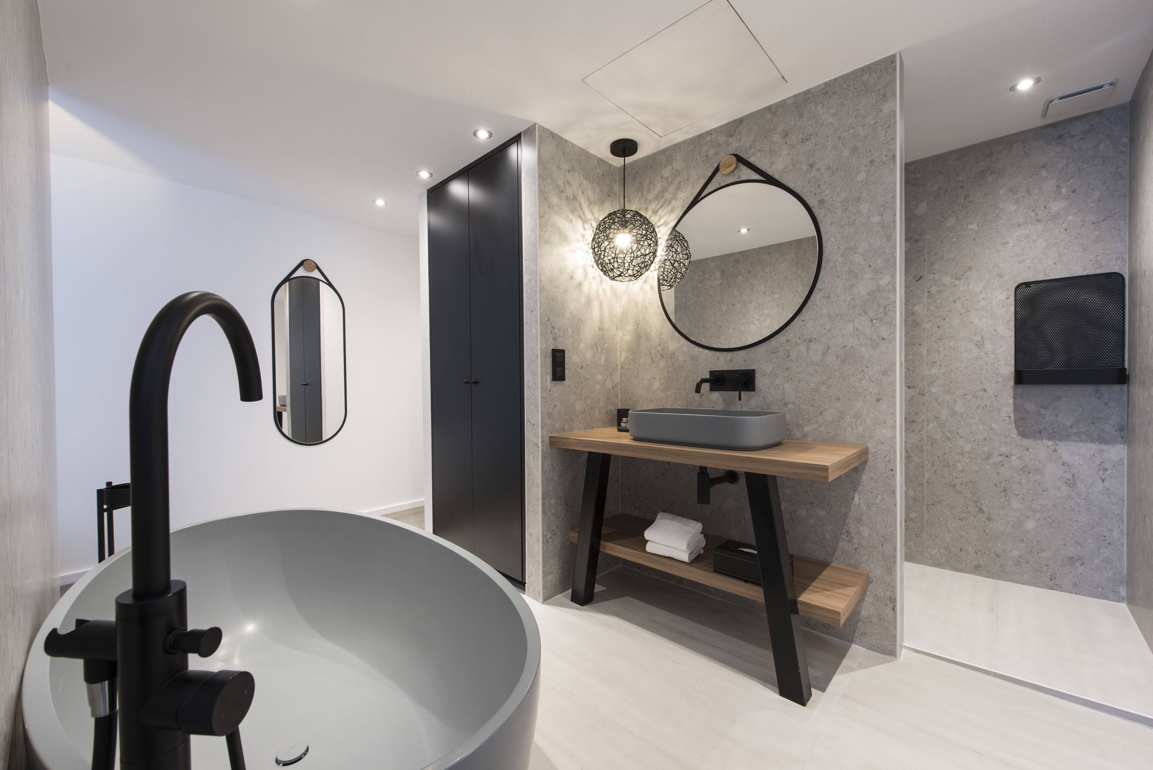 A modern bathroom with a large freestanding bathtub, a minimalist vanity with a round mirror, and a textured wall.