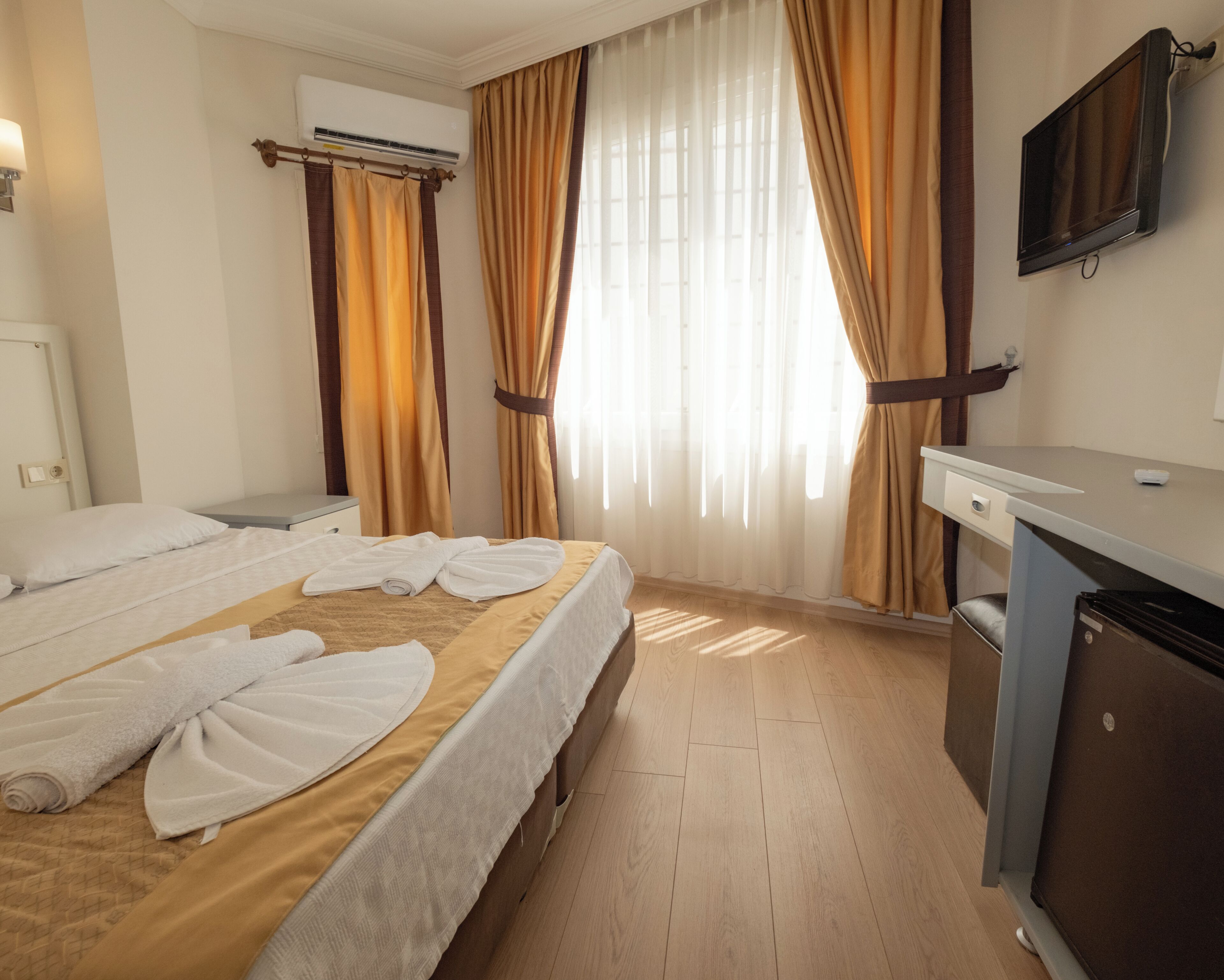 Et hotelværelse med seng, skrivebord, aircondition og fjernsyn.