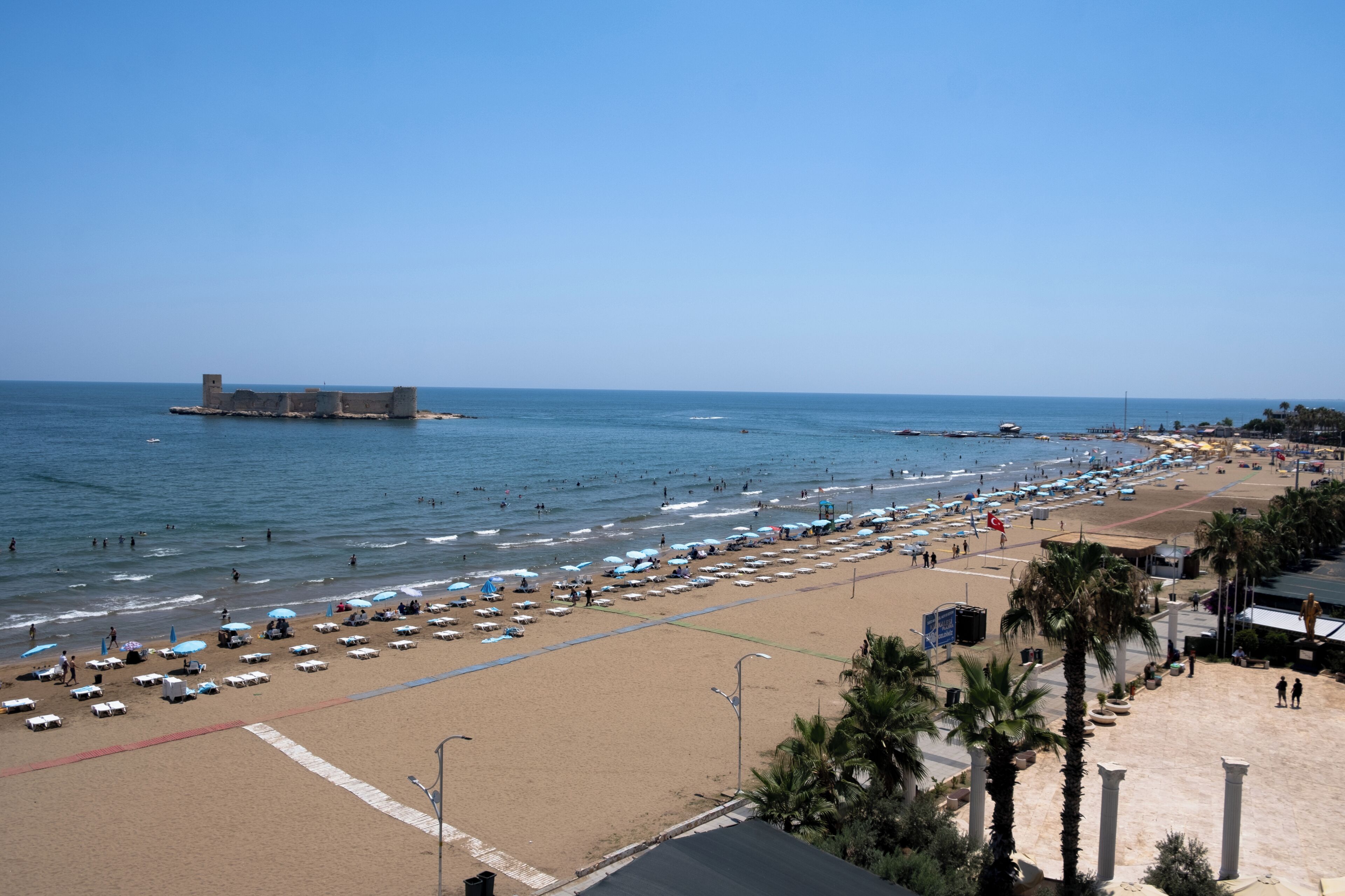 Una playa con sombrillas, sillas de descanso y una fortificación a lo lejos.