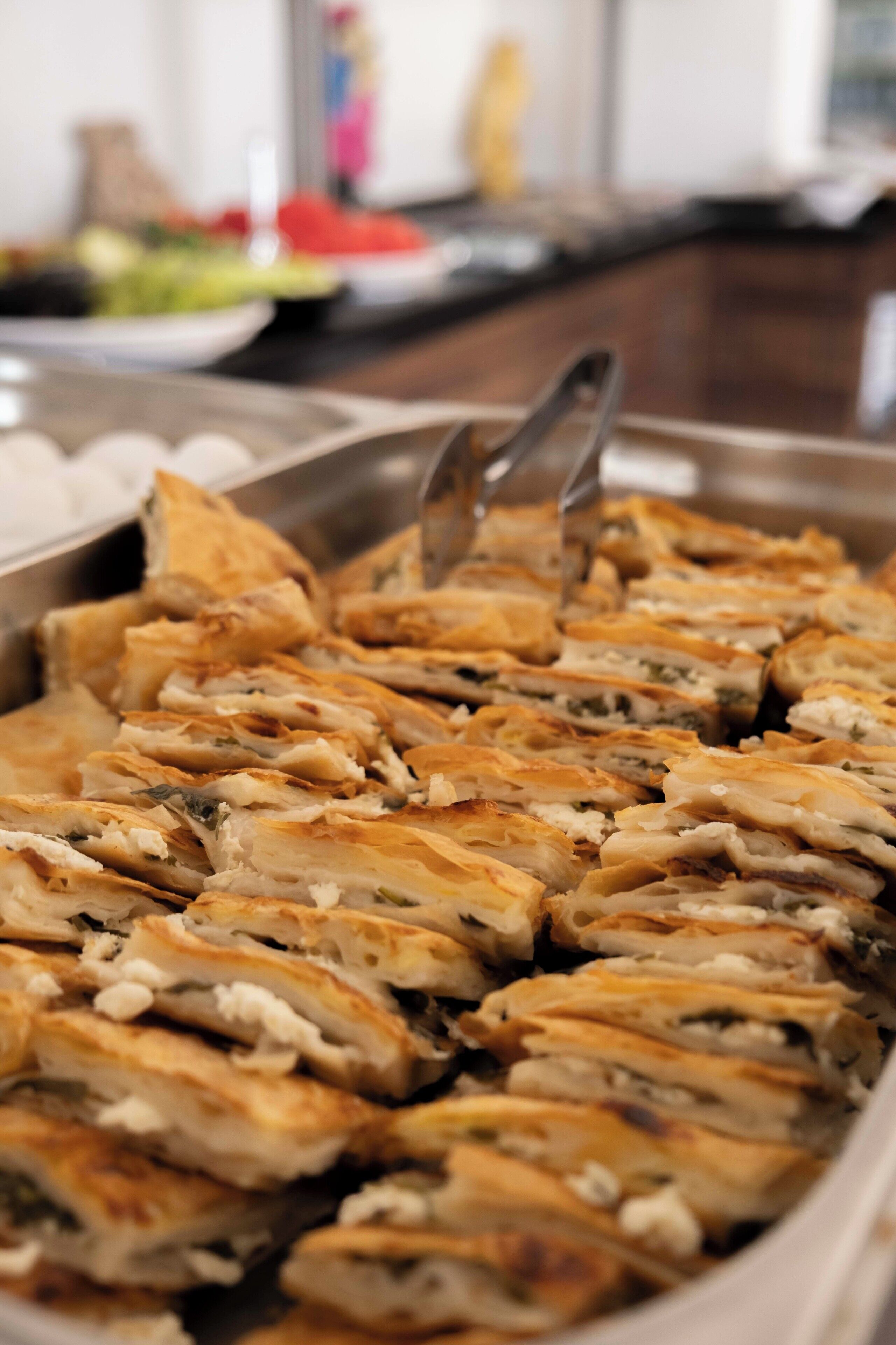 Un bufé con diversos platos, incluyendo una bandeja de pasteles en rodajas de corte dorado.