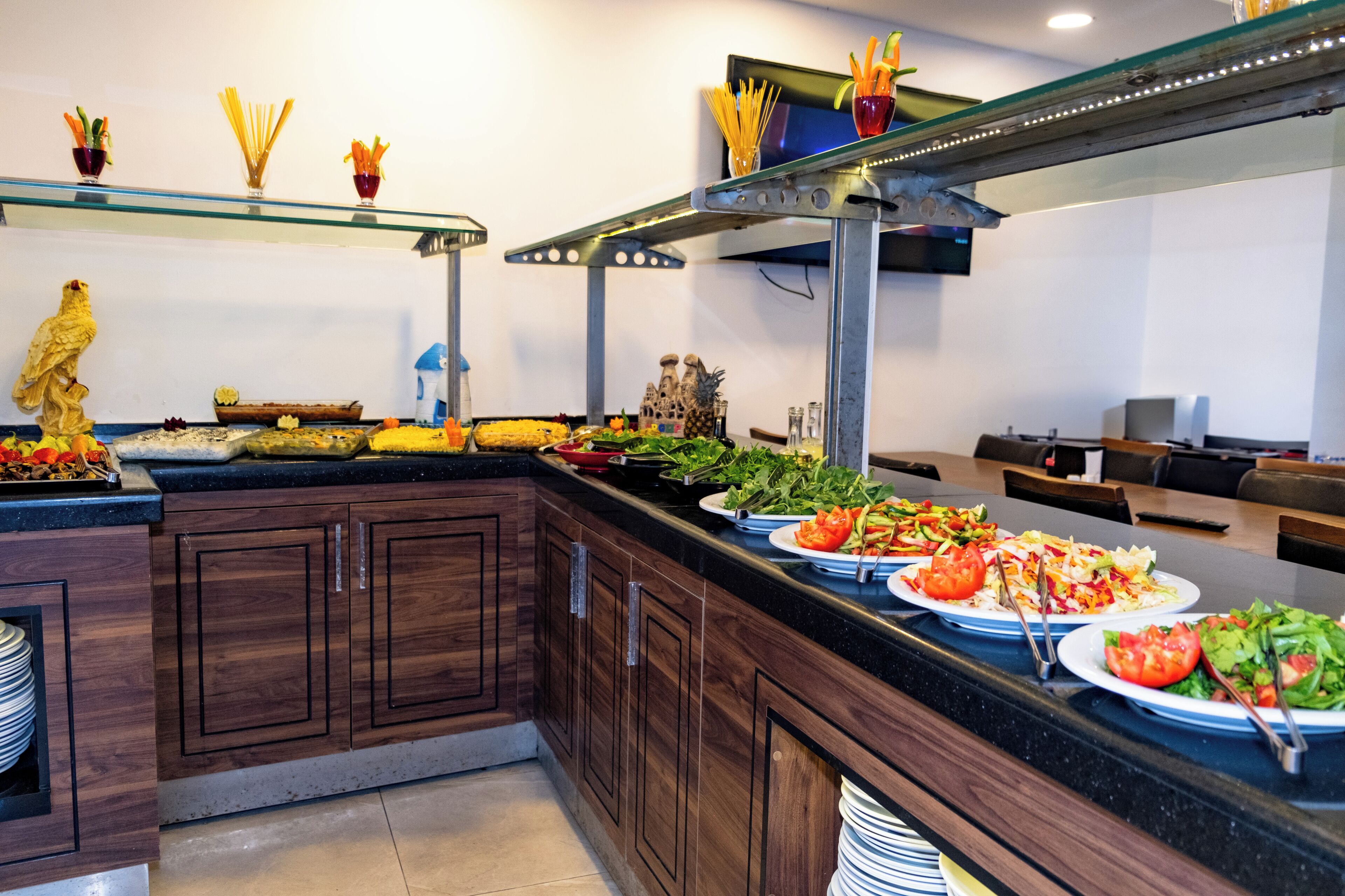 A buffet setup with various food items, a decorative bird statue, and a glass shelf with utensils.