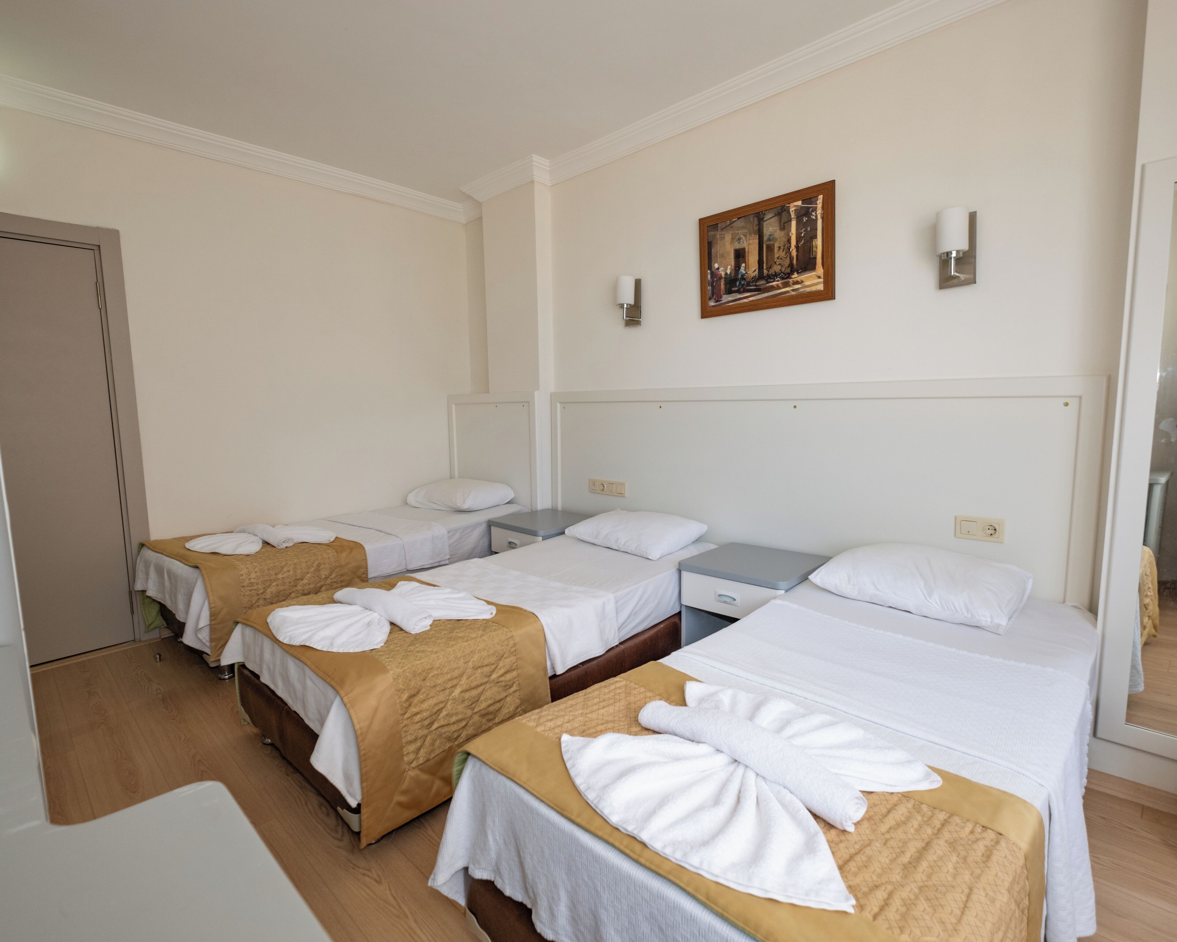 A hotel room with three beds, a painting on the wall, and a bedside lamp.
