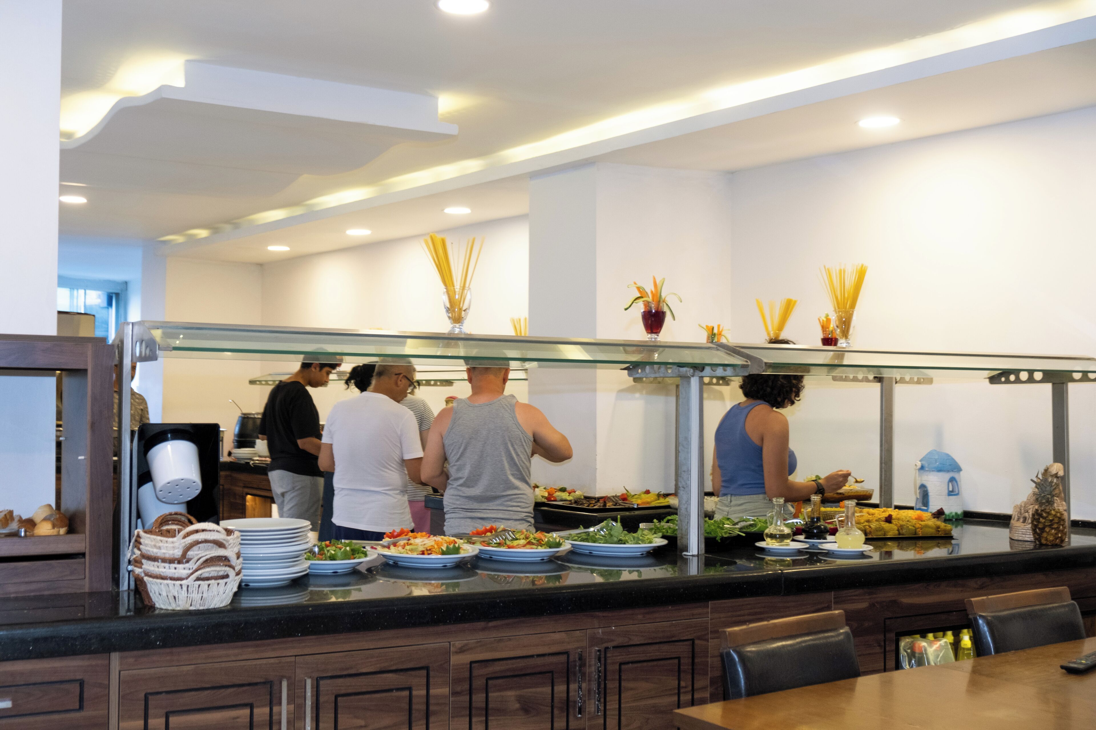 A buffet area with multiple food stations, a glass partition, and a seating area with tables and chairs.