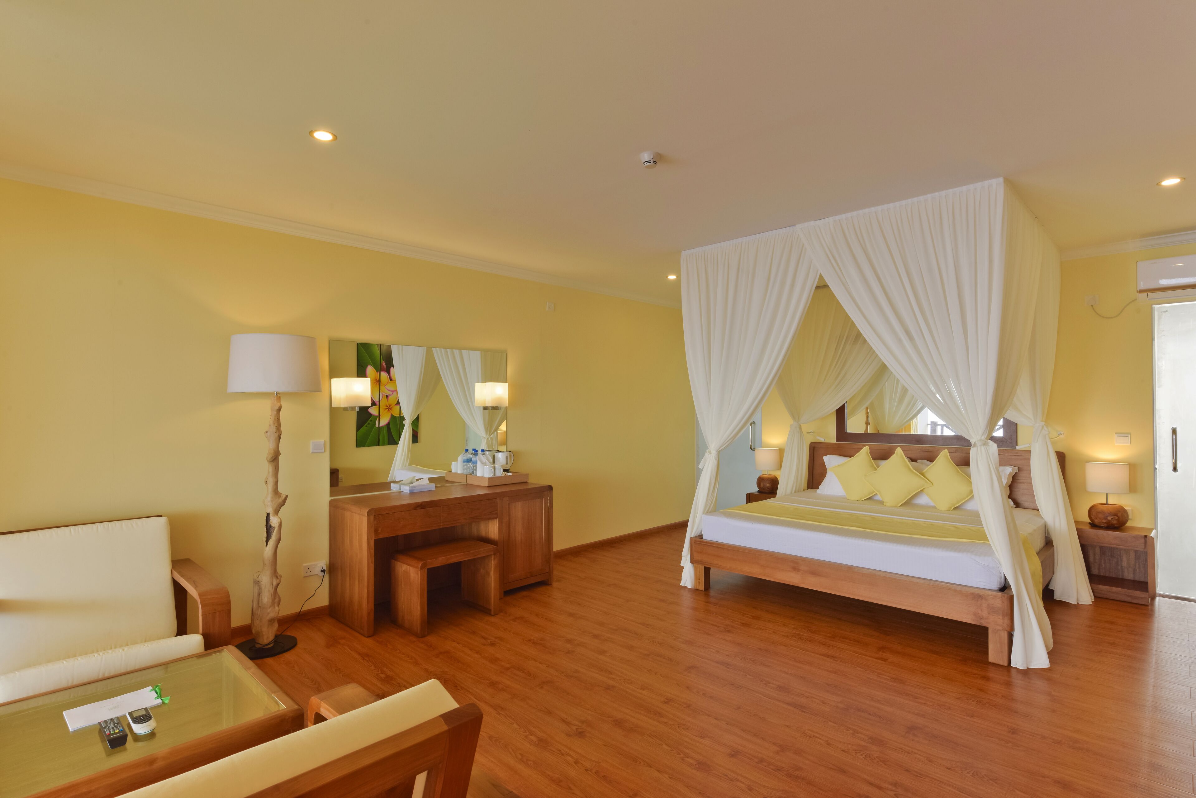 A hotel room with a wooden bed, a desk, a chair, a bedside table, a lamp, and a mirror.