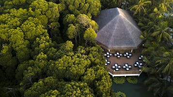 Luftaufnahme eines Resorts mit einer strohgedeckten Struktur, umgeben von dichtem tropischen Grün und Palmen.