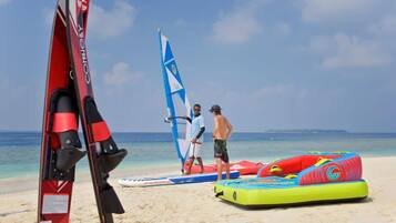 A beach with a windsurfing board, a sail, and inflatable water toys.