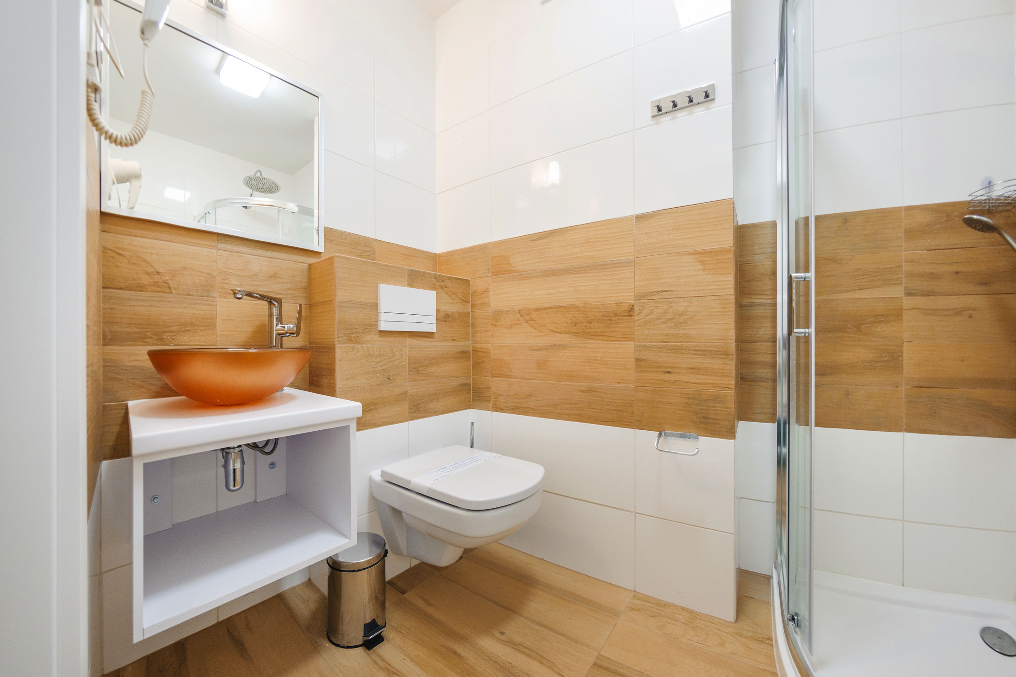 A modern bathroom with a wooden vanity, a white sink, a toilet, and a glass-enclosed shower.