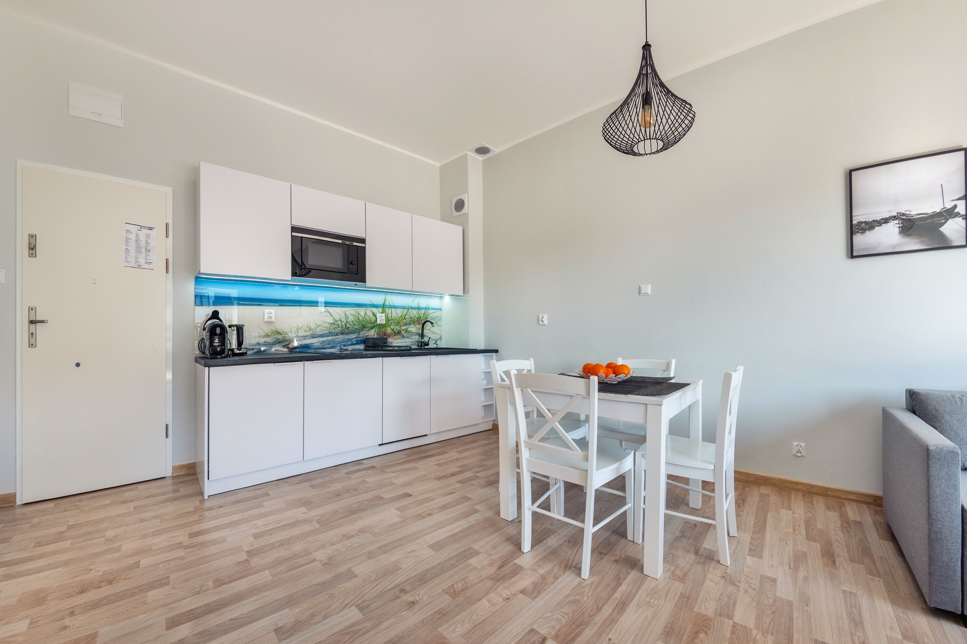 A modern kitchen with white cabinets, a blue backsplash, and a dining area with white chairs.