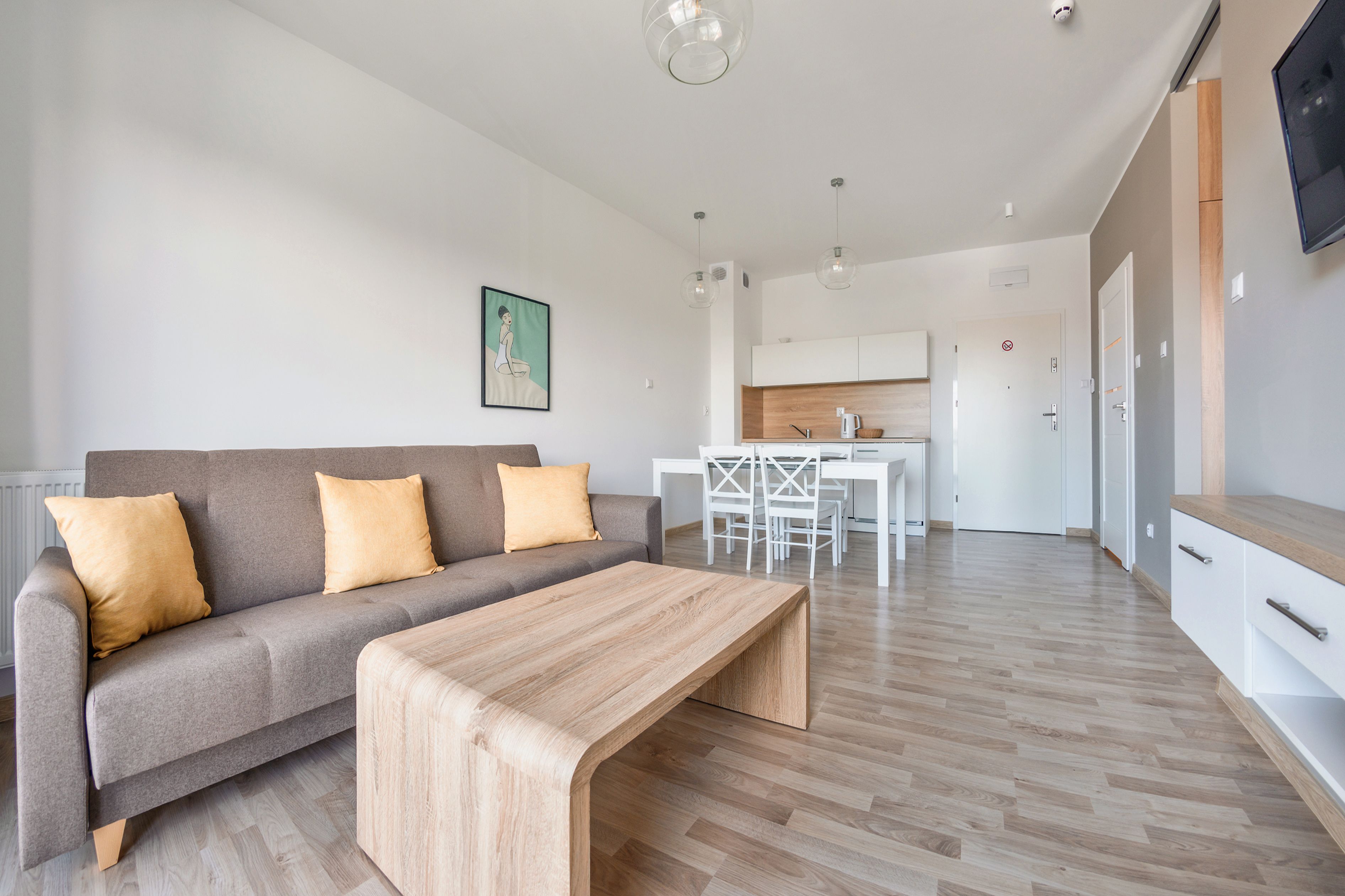 Een moderne woonkamer met een grijze bank, een houten salontafel en een eetgedeelte met witte meubels.