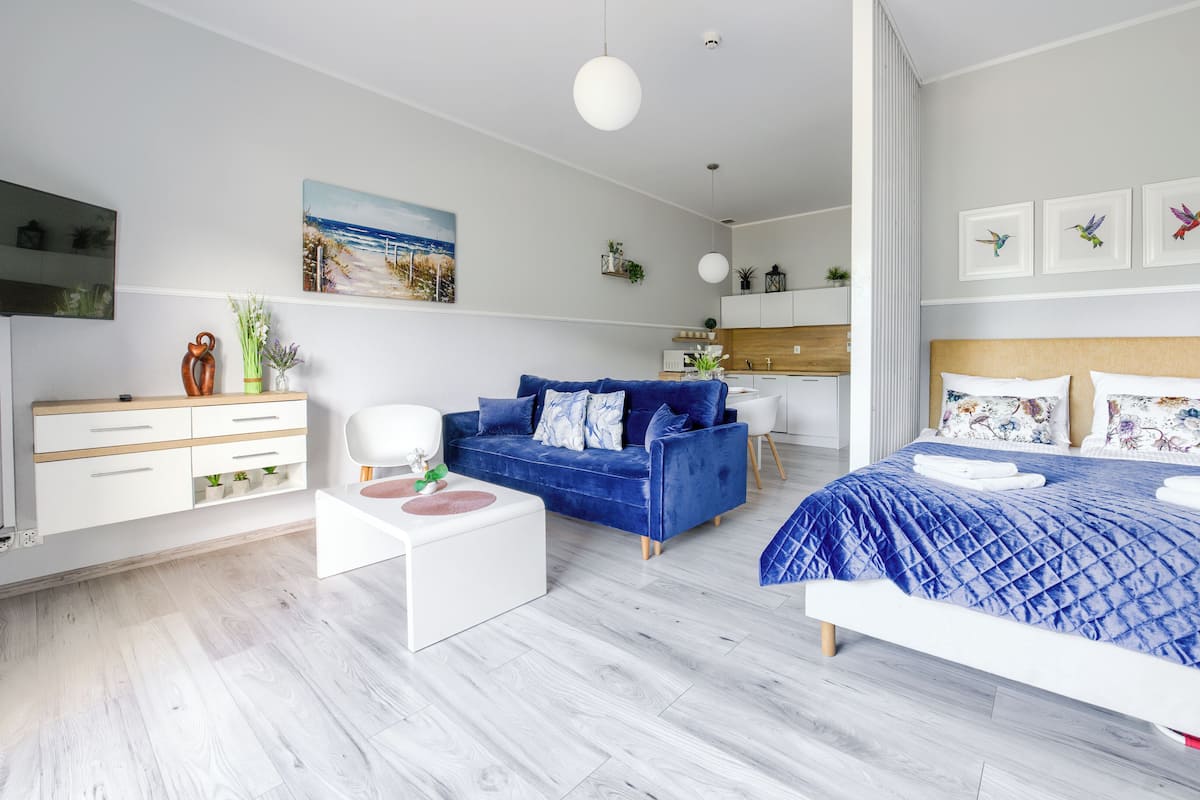 A modern bedroom with a large bed, a blue sofa, a white dresser, and a kitchen area.