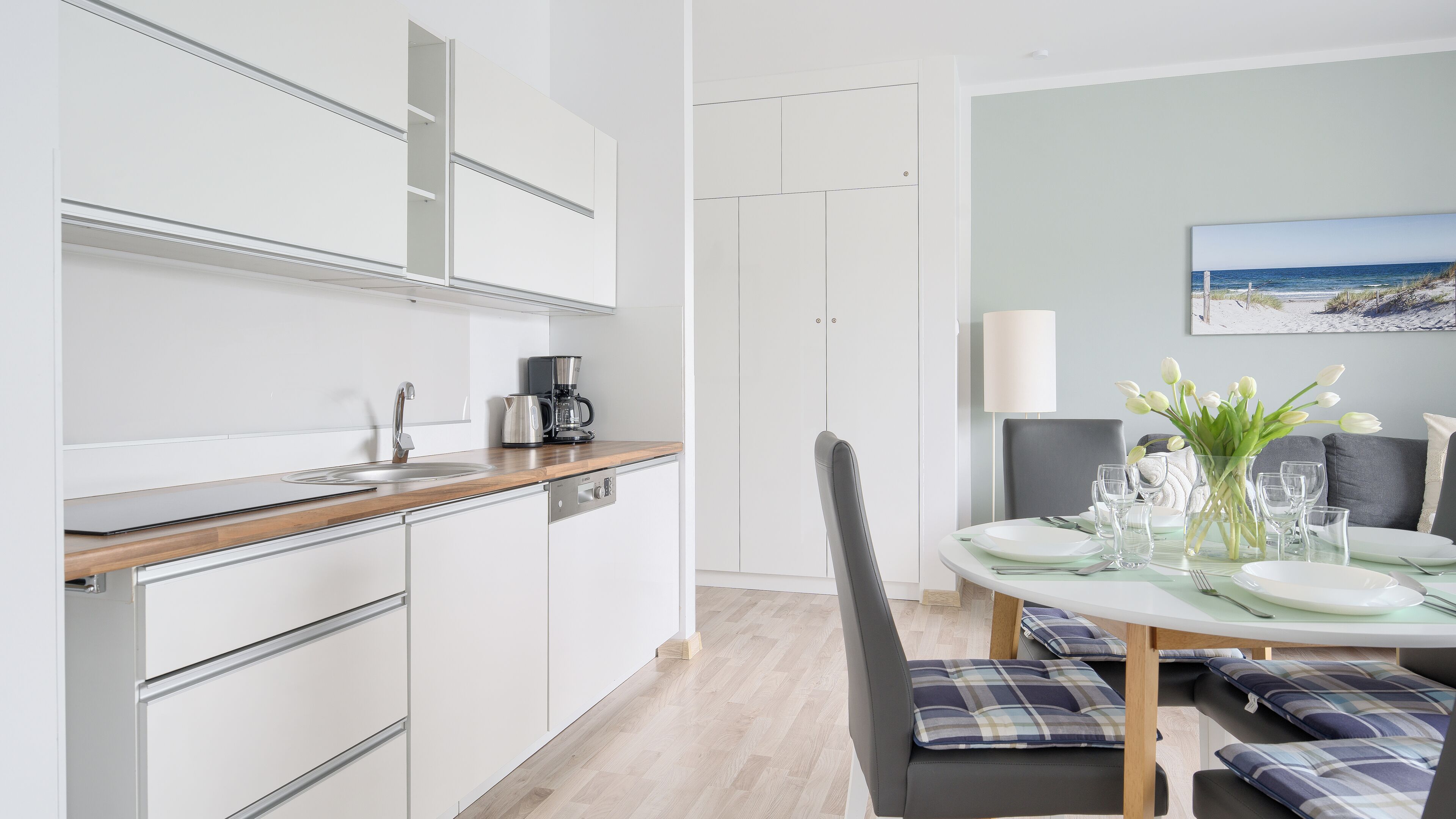 A modern kitchen with white cabinets, a wooden countertop, and a coffee maker.