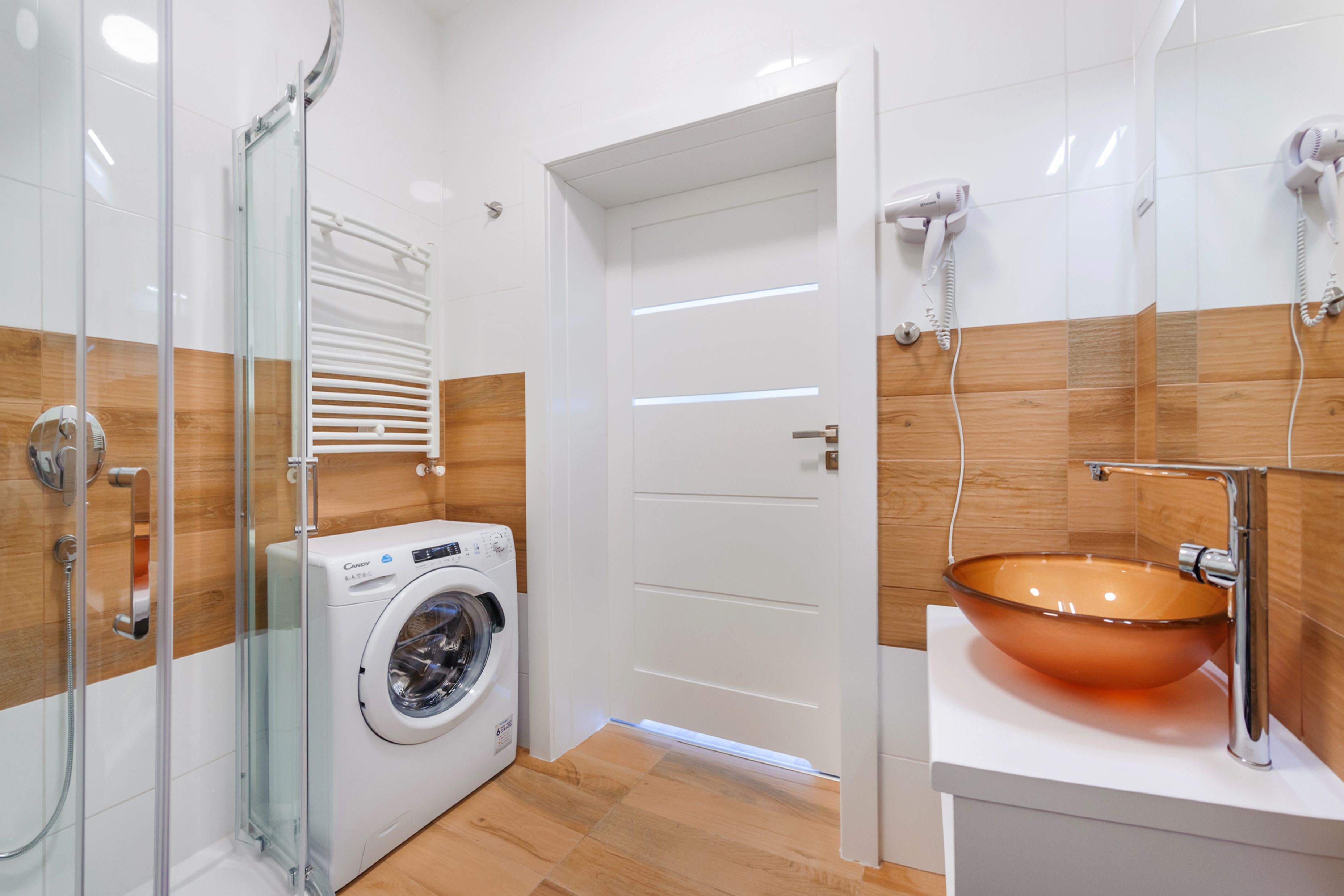 Une salle de bain moderne dotée d’une douche à parois de verre, d’un lave-linge encastré et d’un grand lavabo en verre.