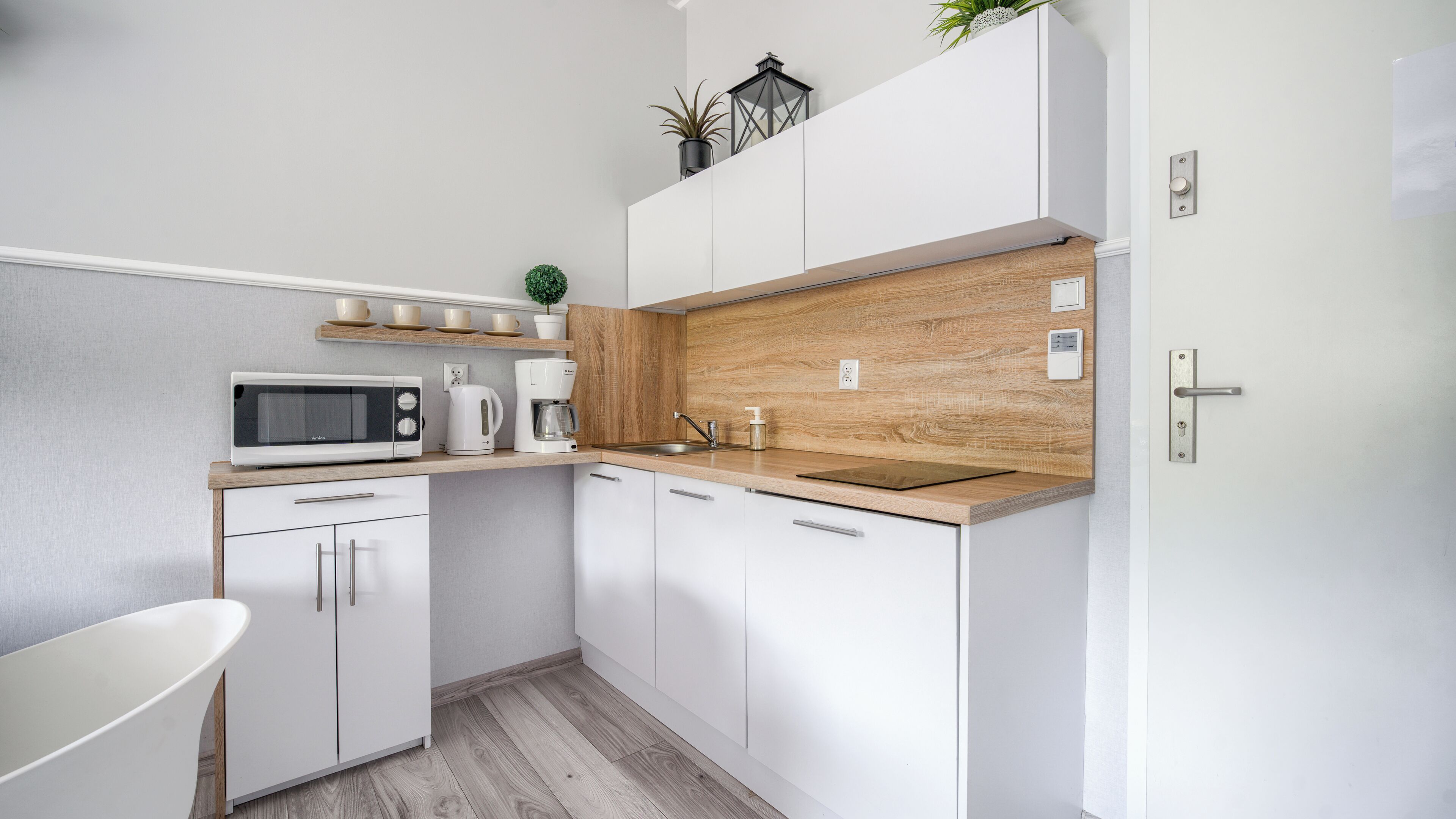 A modern kitchen with white cabinets, a wooden countertop, a microwave, a coffee maker, and a small plant.