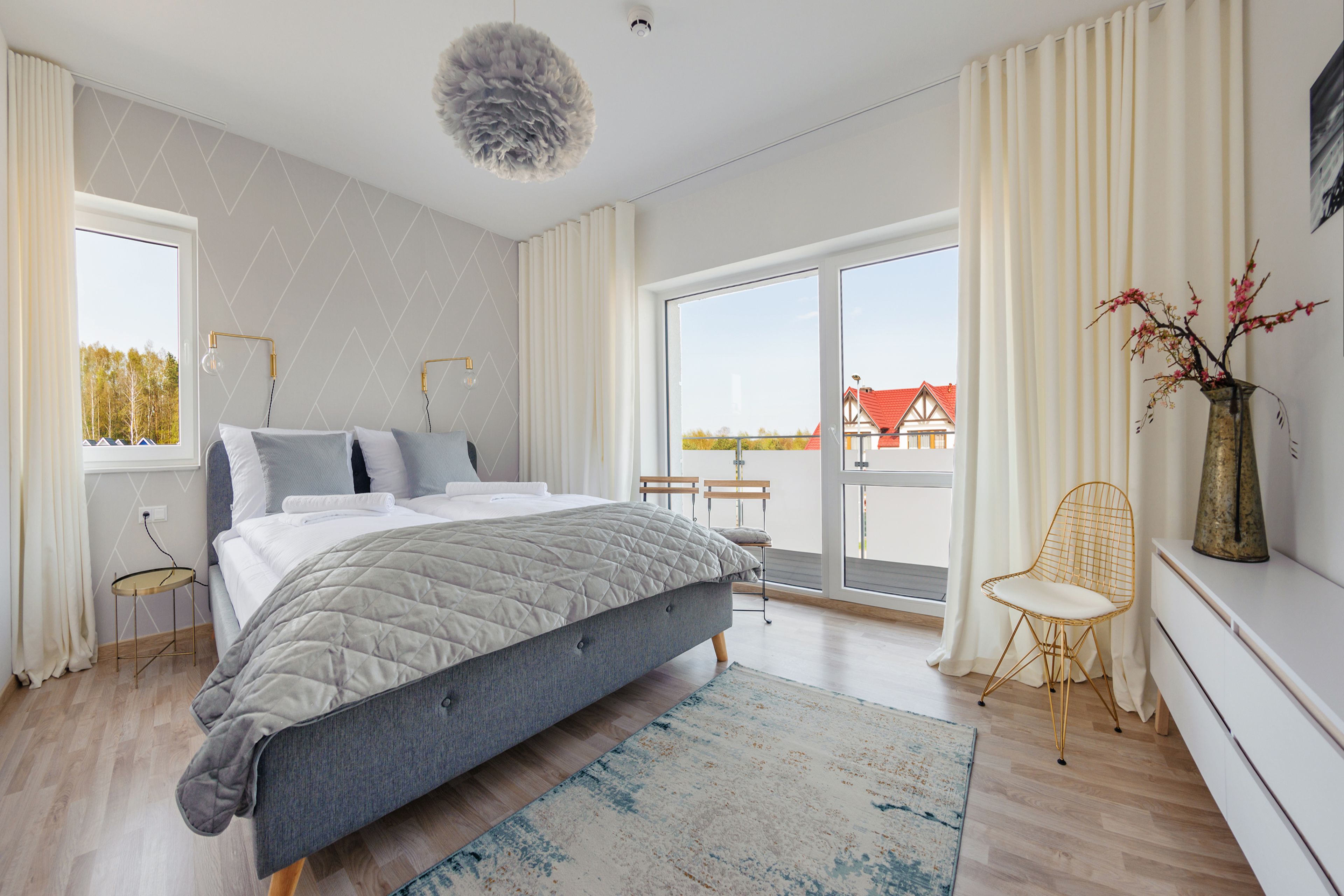 Quarto moderno com uma cama grande, vista exterior, uma mesinha e uma cadeira.