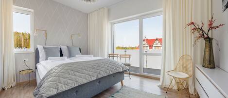 Quarto moderno com uma cama grande, vista exterior, uma mesinha e uma cadeira.