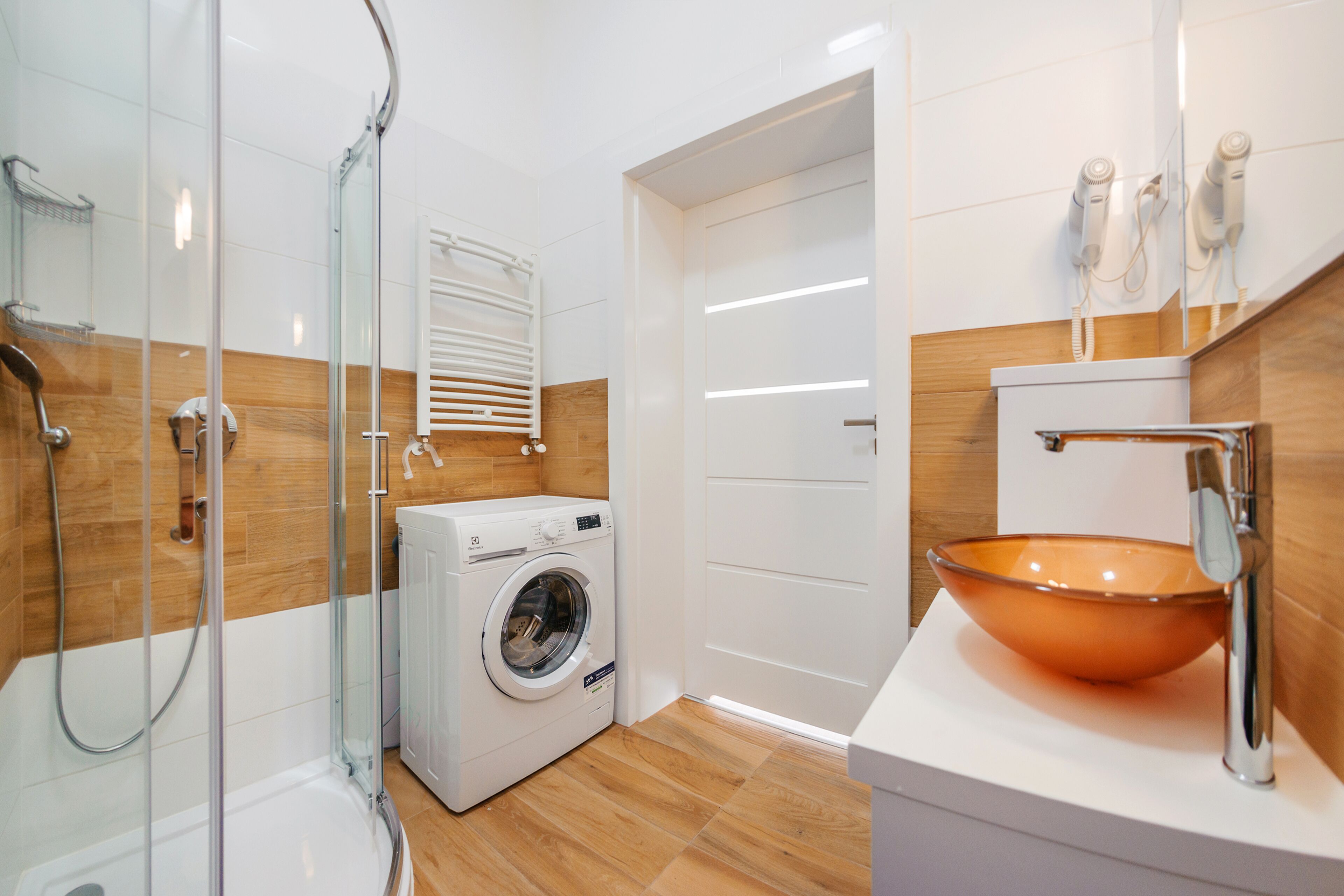 Une salle de bain moderne avec une douche à parois de verre, un lave-linge encastré et un grand lavabo orange.