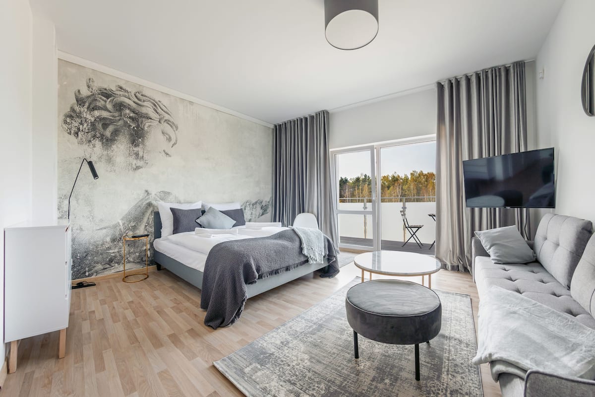 A modern bedroom with a large bed, a sofa, a TV, and a balcony with a view.
