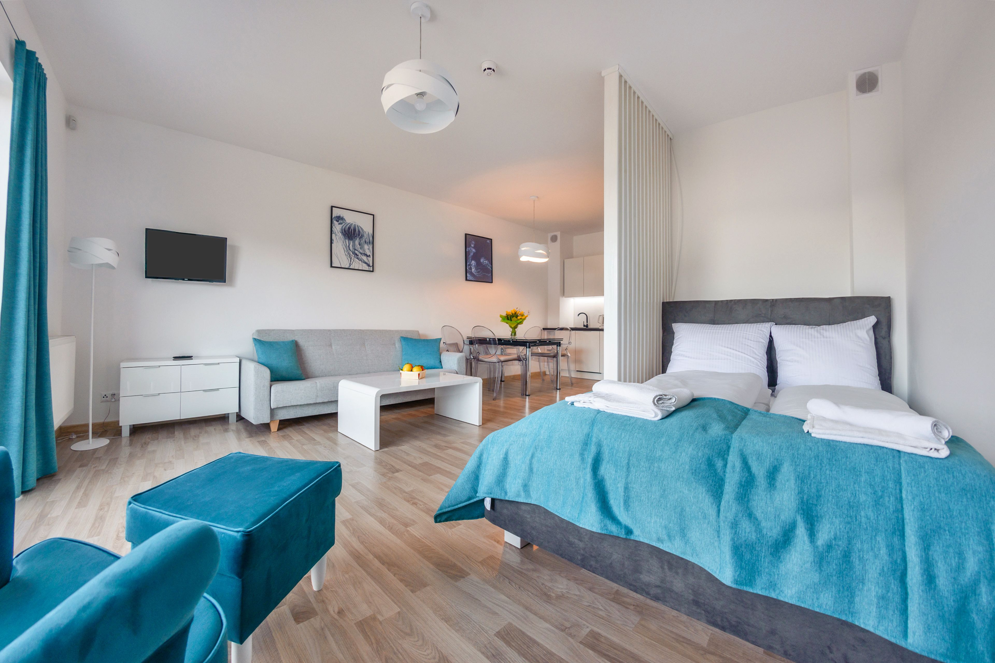 A modern hotel room with a bed, a sofa, a desk, and a dining area.