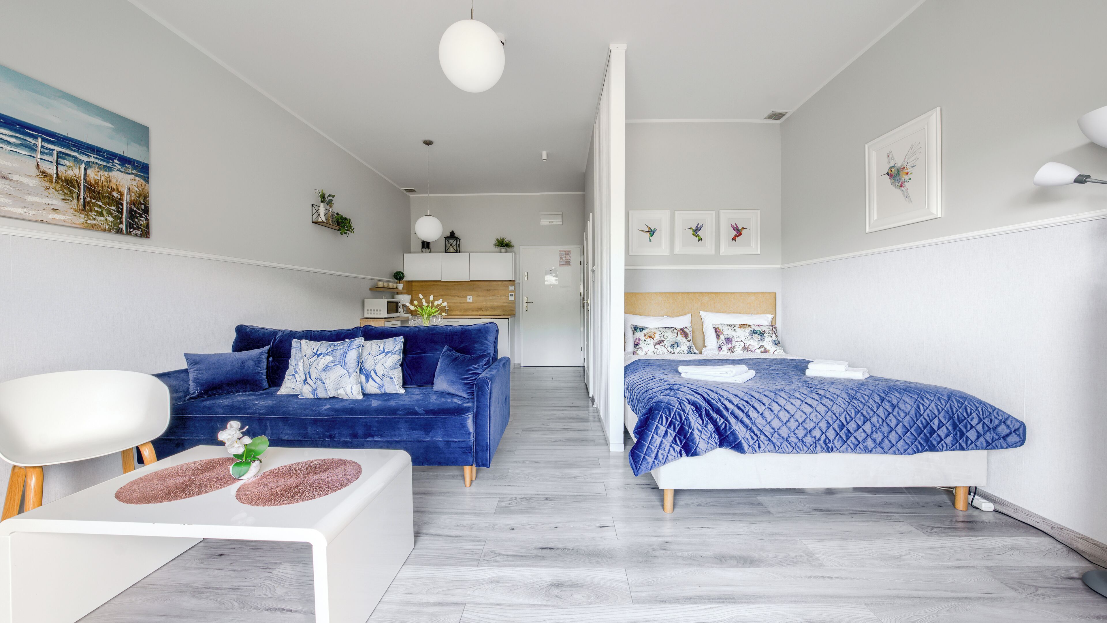 Una habitación de hotel moderna con un sofá azul, una cama con colcha azul y una mesa de centro blanca.