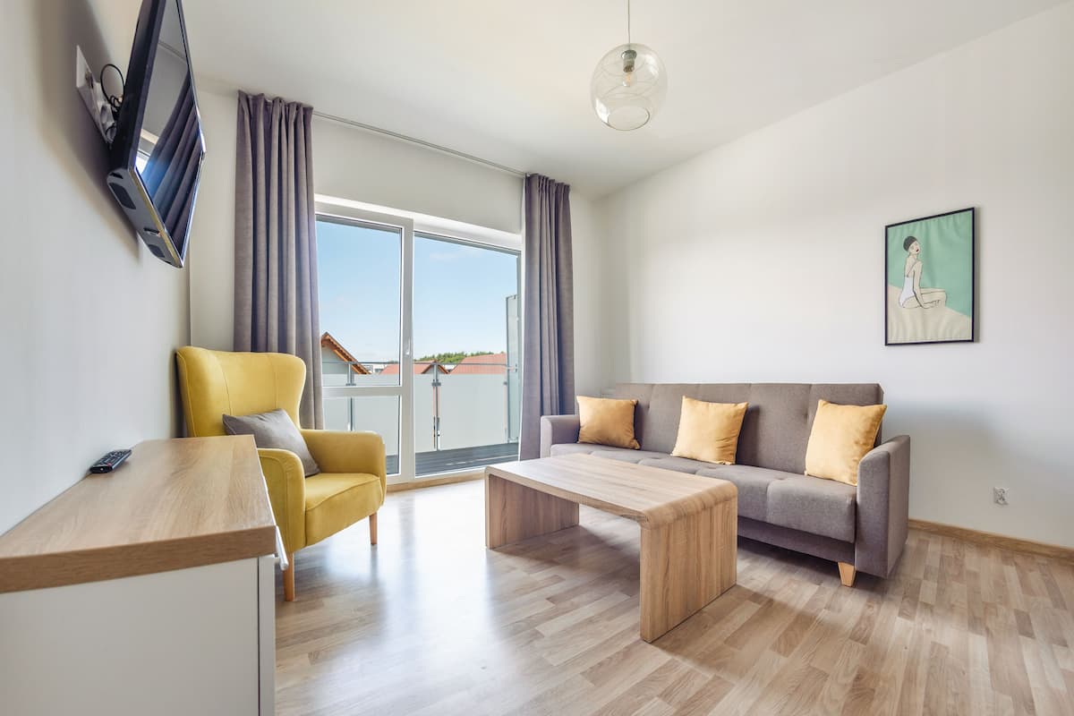 A modern living room with a sofa, a yellow armchair, a wooden coffee table, and a TV mounted on the wall.