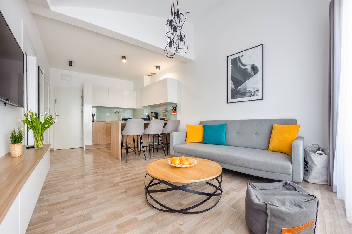 A modern living room with a grey sofa, wooden coffee table, and a kitchen in the background.