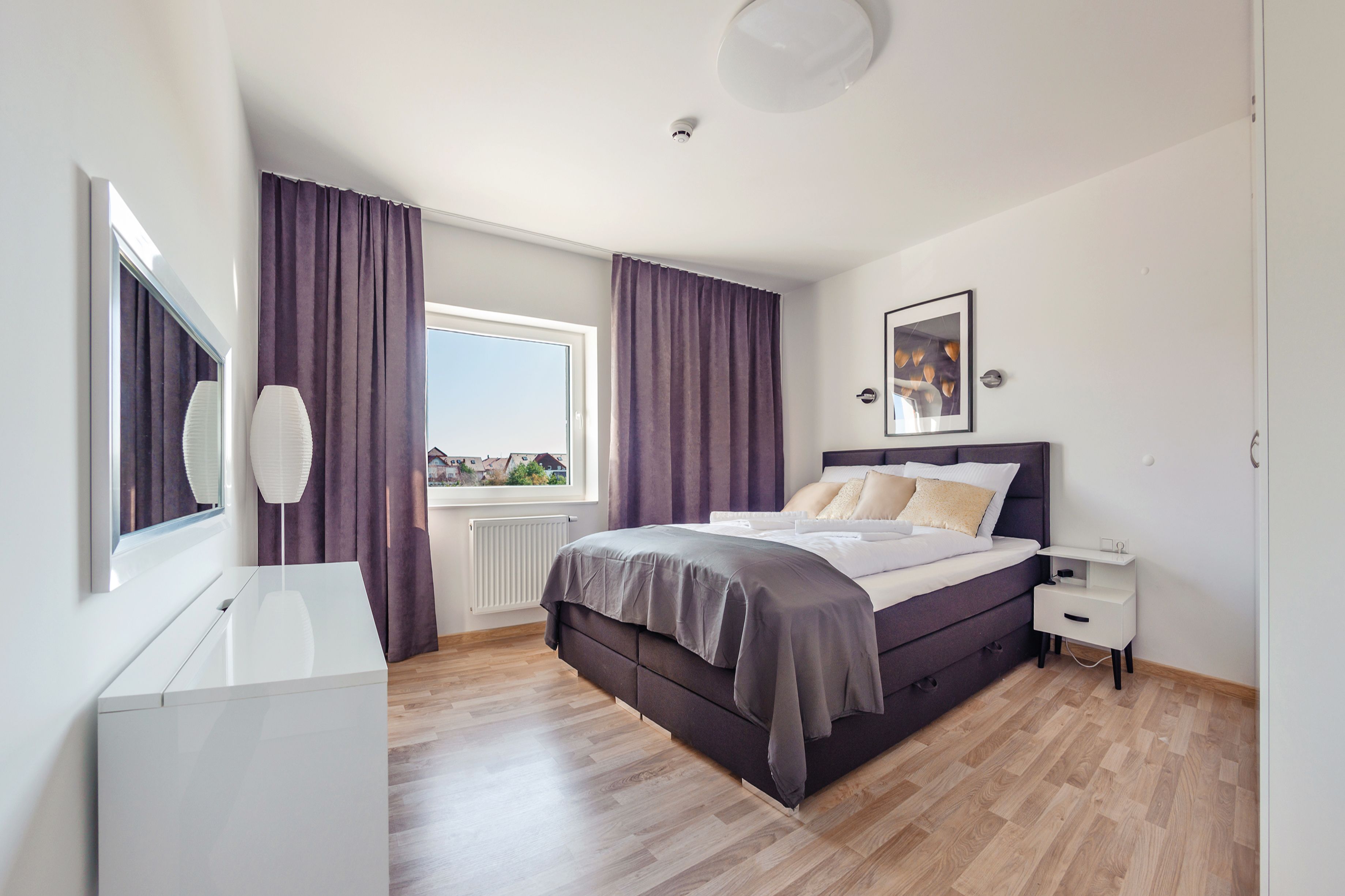 Een moderne slaapkamer met een groot bed, een nachtkastje, een dressoir en een raam met gordijnen.