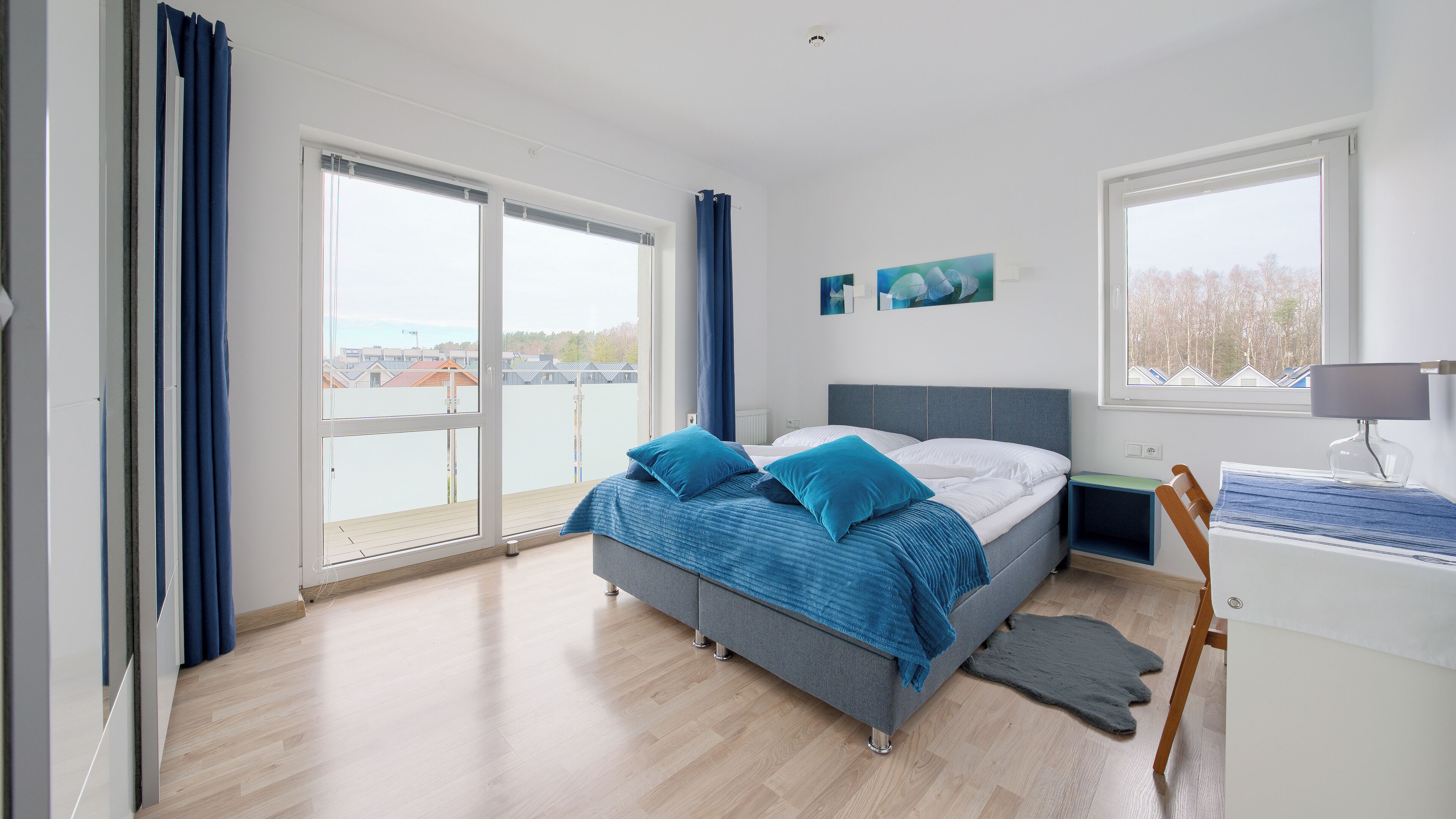 Une chambre à coucher avec un lit, un bureau, une chaise et de grandes fenêtres.