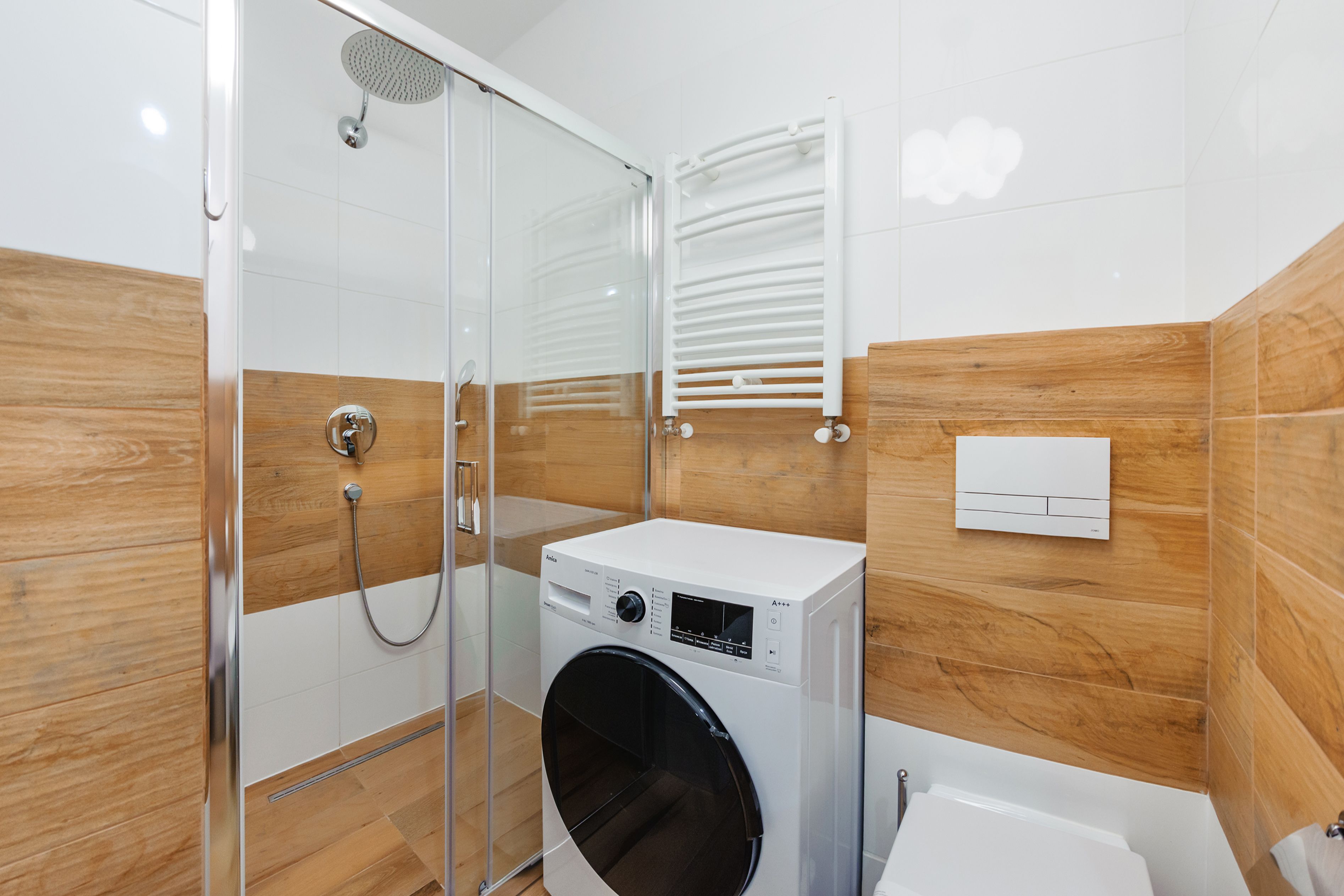 A modern bathroom with a glass shower enclosure, a built-in washing machine, and a white toilet.